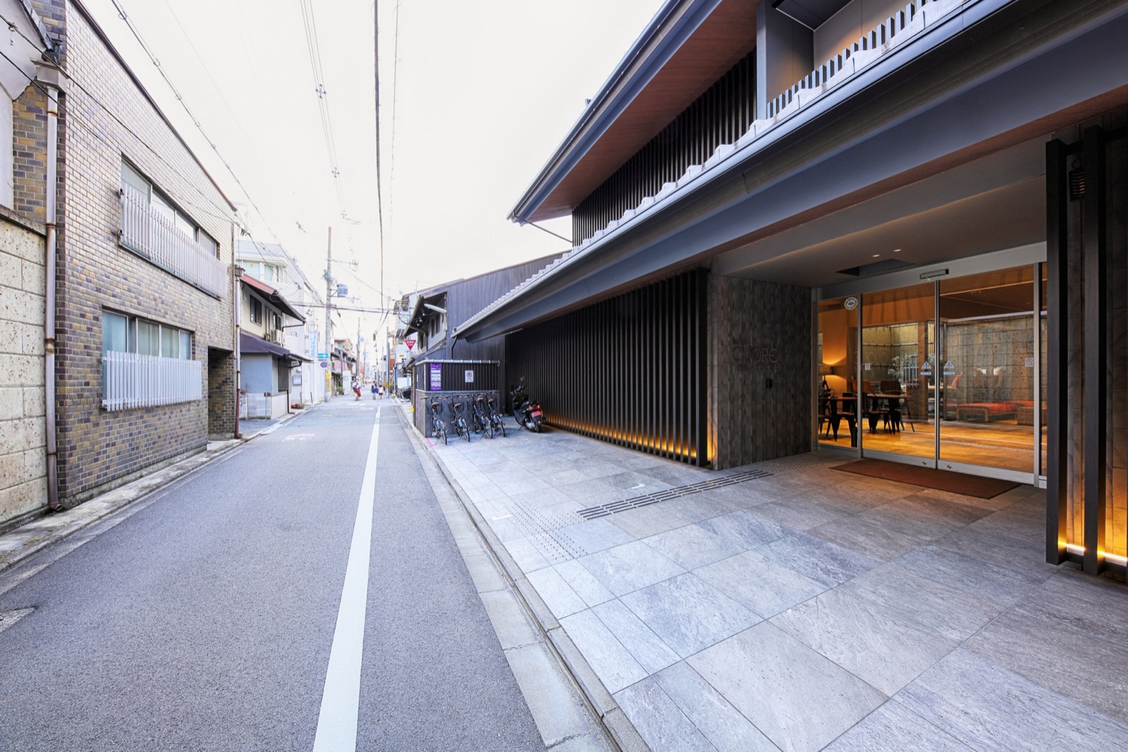 ホテル前の路地。左手に住宅が並び、右手に黒い木格子の外観と駐輪スペースが続く